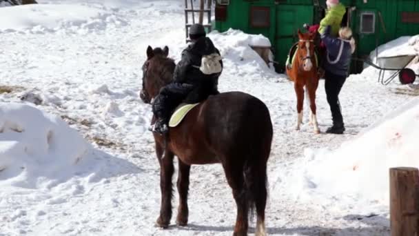 Хлопчик сидить на коні, жінка допомагає своїй сестрі лізти на коні — стокове відео