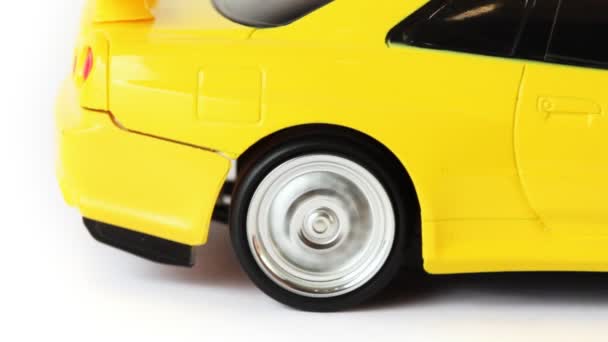 Rear wheel of yellow toy radio-controlled car slips on white background — Stock Video