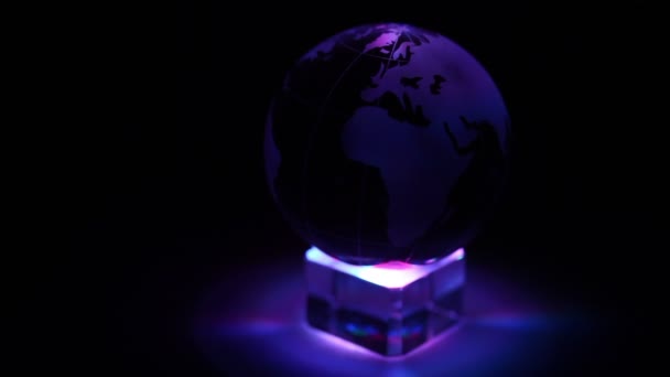 Glazen bol van de aarde draait op kubus met kleur verlichting — Stockvideo