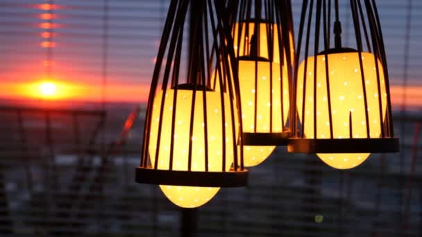 Fyra lampor hänger innan persienner där solnedgången är synlig — Stockvideo