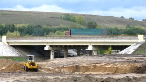 Pelle niveau terre pour la construction de la route en face du pont automobile — Video