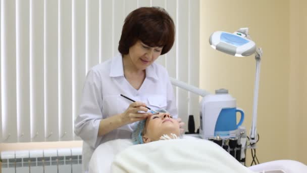 Woman lies and Cosmetician colors eyebrows of patient by brush — Stock Video