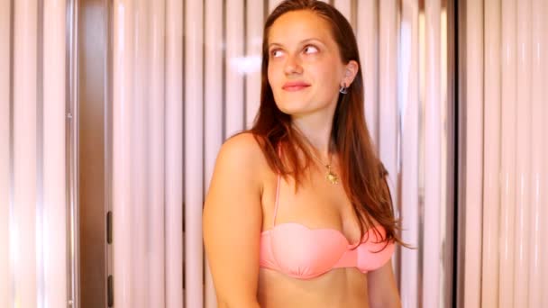 Молодая женщина загорает в купальнике в вертикальном солярии возле панели управления — стоковое видео