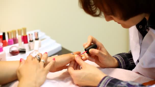 Косметик аккуратно покрывает ногти клиента розовым лаком для ногтей в салоне — стоковое видео