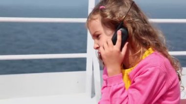 küçük kız oturuyor ve çitin yanında güvertede cep telefonuyla konuşuyor