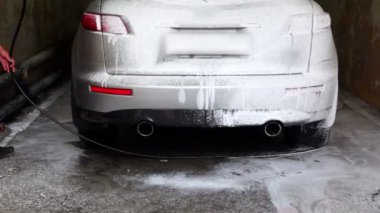 Adam araba etrafında yürüyüş ve köpük carwash hortum tarafından kapak