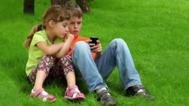 iki çocuk birlikte oturup, çocuk cep telefonuyla dijital oyun oynuyor