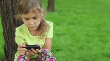 Kız cep telefon ekranında ağaç çim ve seyretmek karşı eğilir
