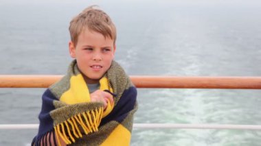 Halıya sarılmış küçük çocuk güvertede yolculuk sırasında duruyor.