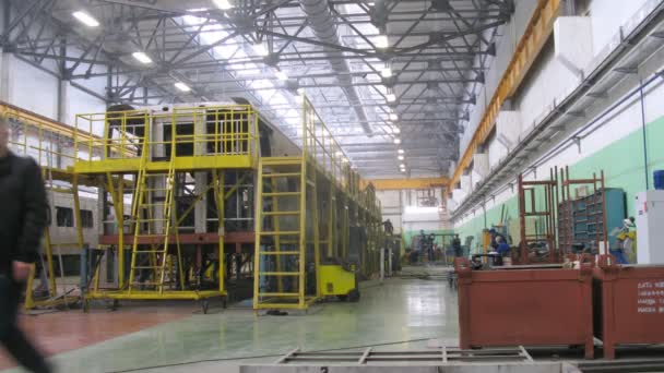 Рабочие идут по железным лестницам рядом с новой каретой на заводе — стоковое видео