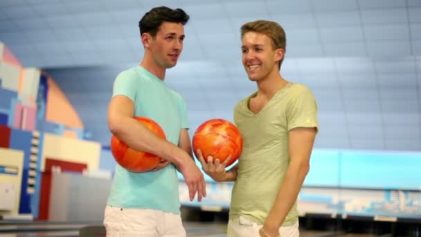 Twee vrienden staan in bowlingclub met ballen en praten — Stockvideo