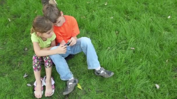 Sister watches how brother plays with digital game on cell phone — Stock Video