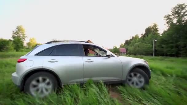 Человек в машине ездит по траве, на заднем плане деревни — стоковое видео