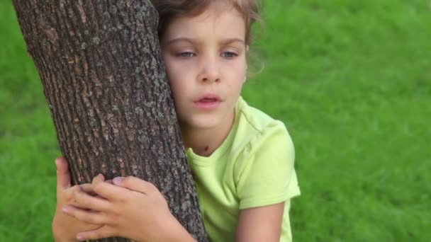 Little girl embraces tree and speaks, closeup view at summer day — Stockvideo