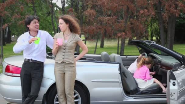 Les parents se tiennent avec des lunettes près du cabriolet, les enfants jouent en voiture — Video