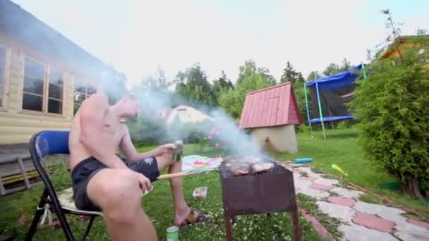 Mann sitzt im Rauch und kocht Dönerspieß auf Grill in der Nähe von Landhaus — Stockvideo