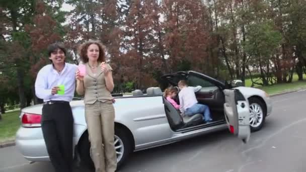 Parents eat near cabriolet and their kids play in car — Stock Video