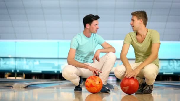 Два студента сидят и крутят шары на фоне боулинга — стоковое видео