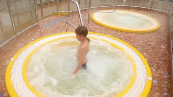 Two kids sit in pool with hot water, mother stands near — Stock Video