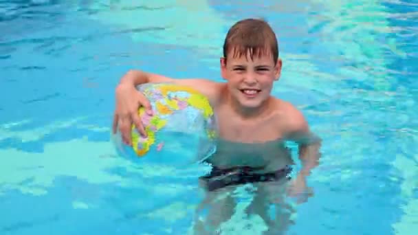 Kleine jongen staan in zwembad en houd opgeblazen bal — Stockvideo