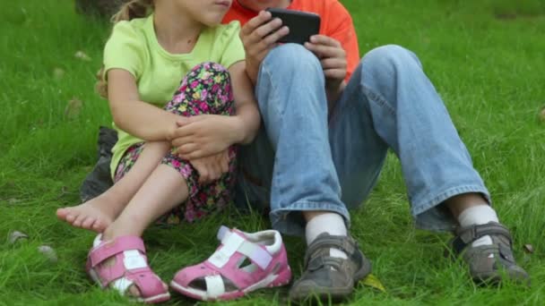 Два ребенка мальчик и девочка сидят вместе на траве возле парковки — стоковое видео