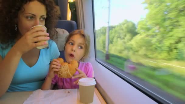 Mamma dricker kaffe och dotter äter när de reser i tåg — Stockvideo