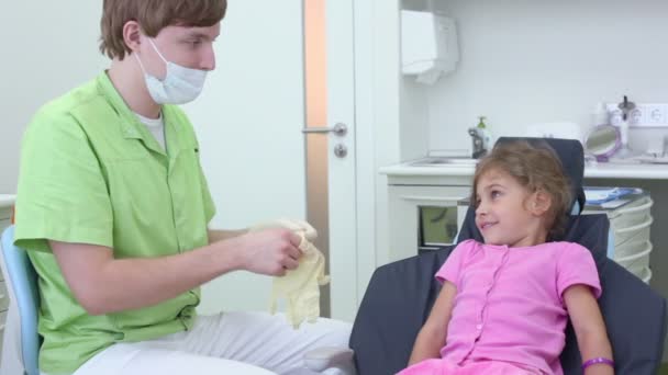 Dentista coloca luvas e menina vê-lo da cadeira dentária — Vídeo de Stock