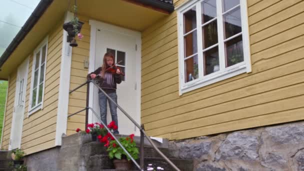 Niña toca en violín para turista en porche de casa — Vídeos de Stock