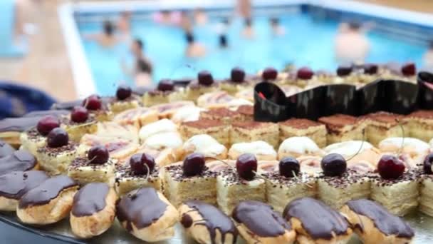 Prato cheio de bolos doces e eclairs em frente à piscina — Vídeo de Stock