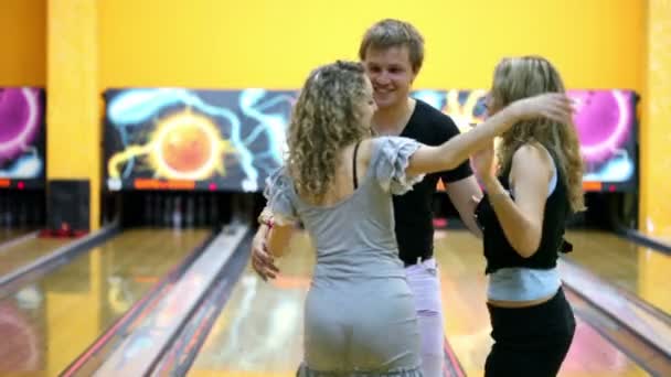 Две девушки с одним парнем танцуют рядом в боулинг-клубе — стоковое видео