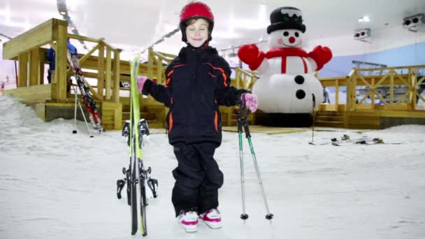 Little girl in warm clothes and helmet stands with skis — Stock Video