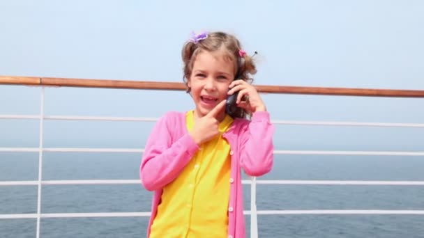 Маленькая девочка стоит и разговаривает по мобильному телефону на палубе возле забора — стоковое видео