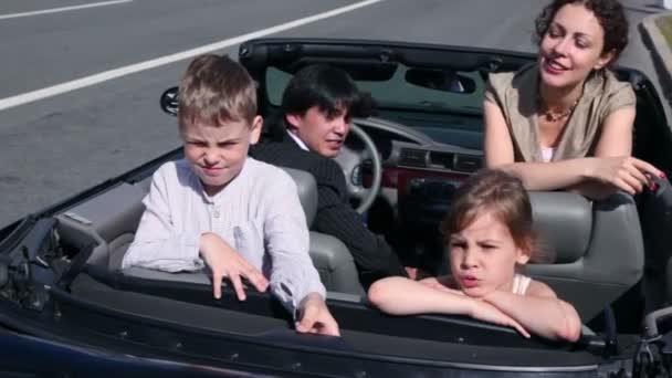 Los padres y dos niños se sientan en el coche y se van en un día soleado — Vídeo de stock