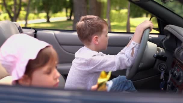 Barnen sitter i cabriolet, flicka lekar och bror håller föraren hjulet — Stockvideo