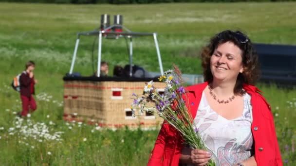 Woman stands in front of basket of balloon and holds bouquet — Stock Video