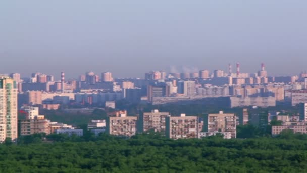 Ağaçlar ve endüstriyel borular arasında evleriyle şehir panoraması — Stok video