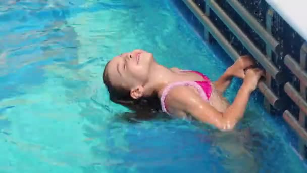 Little girl holds by tube at pool edge and plunges in water — Stock Video