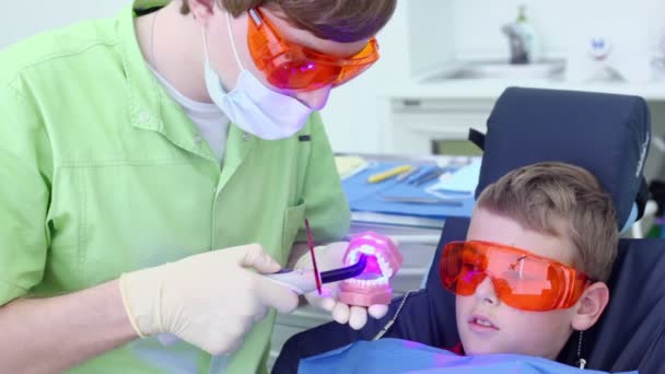 El dentista sostiene la mandíbula y usa la luz para endurecer el relleno cerca del niño — Vídeos de Stock