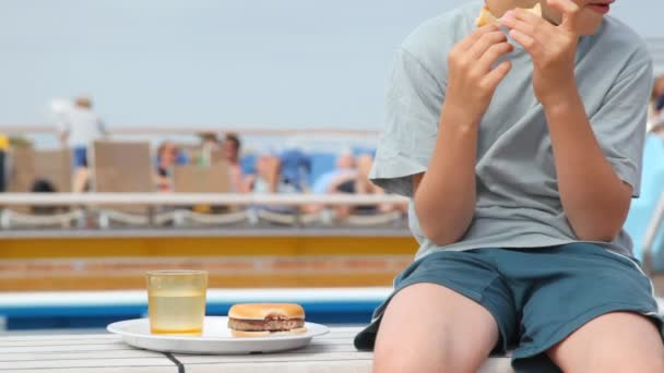 Junge sitzt neben Teller mit Hamburger, isst und trinkt — Stockvideo