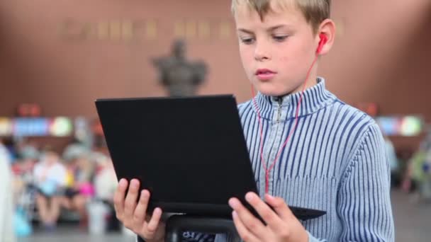 Liten pojke håll netbook när sitter på tågstationen — Stockvideo