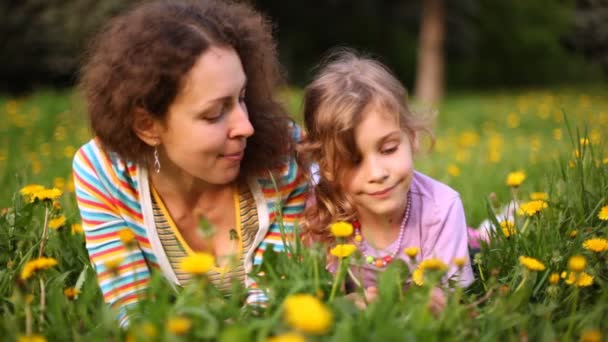 Mother and daughter lie on green glade with yellow dandelions — Stock Video
