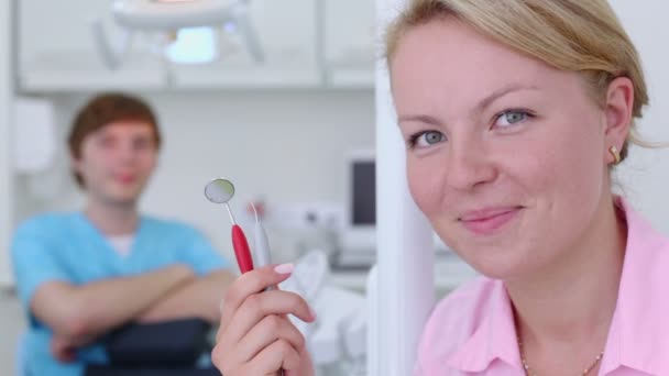 Infirmière avec des sourires d'outil dentaire et le médecin est assis derrière unfocused — Video