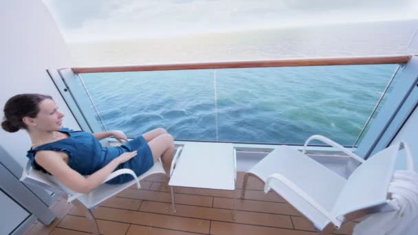 Женщина сидит на стуле перед столом в огороженной части палубы корабля — стоковое видео