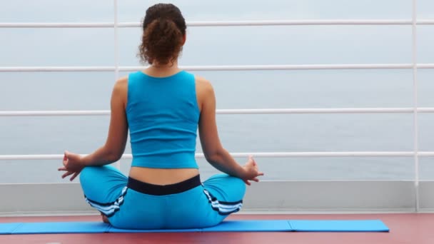 Vrouw zit terug op het schip dek in lotus pose — Stockvideo