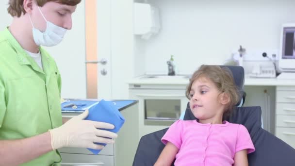 Дантист покрывает девушку, которая сидит на стуле в стоматологической хирургии — стоковое видео