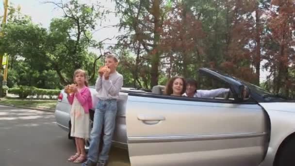 Dwoje dzieci jeść chleb w pobliżu kabriolet, rodzice siedzą w Cabrio — Wideo stockowe