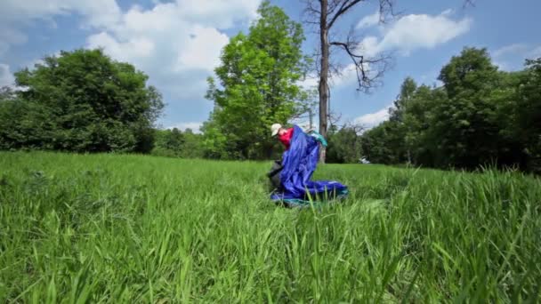 Kleine jongen kampeerplaatsen tent op gras glade onder de blauwe hemel — Stockvideo