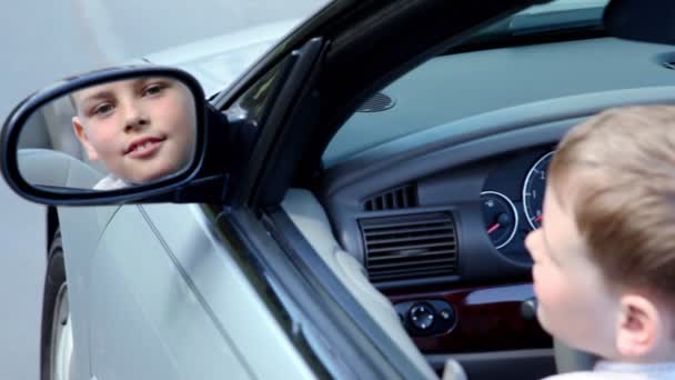 Little boy watches in rear-view car mirror from driver place — Stock Video