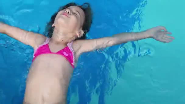 Little girl lies on her back and swims in pool water — Stock Video