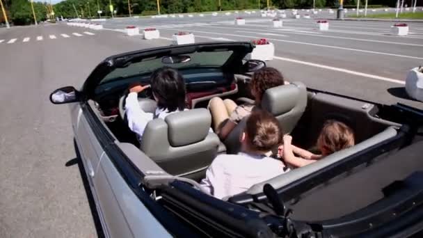 Parents and two kids sit in cabriolet and ride by road — Stock Video